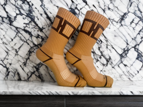 A pair of caramel-colored Hill Toe socks with mocha accents, displayed against a marble background.