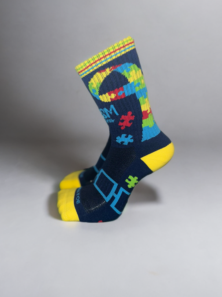 A pair of colorful athletic socks with a puzzle piece pattern and autism awareness ribbons on a white background.